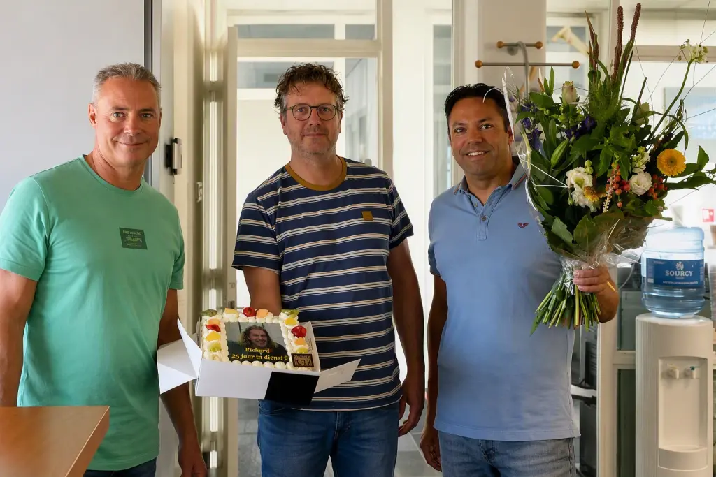 Richard Otto op kantoor bij Bek bv met twee collega's, een jubileumtaart met "Richard 25 jaar in dienst" en een bos bloemen